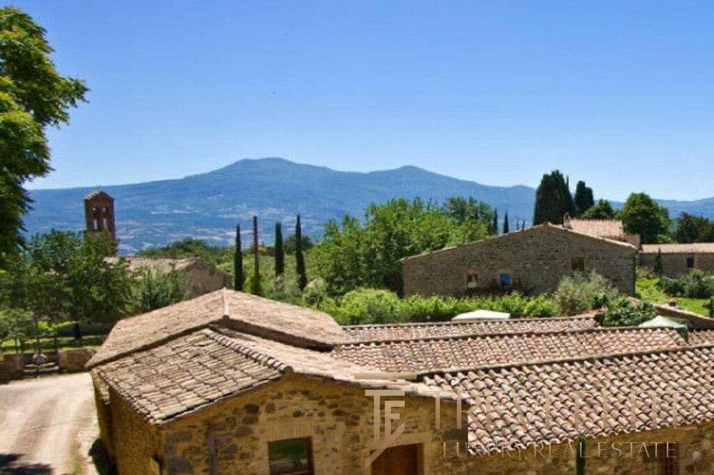 Восхитительный вид на итальянский деревенский пейзаж с крытыми черепичной кровлей домами и зеленью, окружёнными горами и кедровыми деревьями.