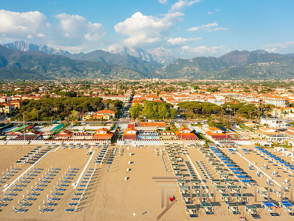 Пляж с шезлонгами и зонтиками на берегу моря на фонегорода и горных вершин, солнечный день.