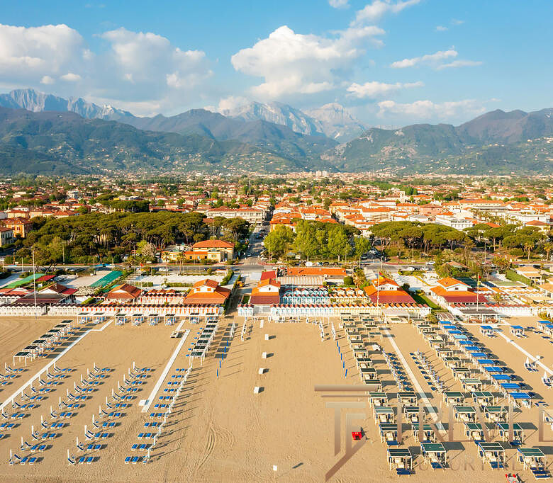 Пляж с шезлонгами и зонтиками на берегу моря на фонегорода и горных вершин, солнечный день.