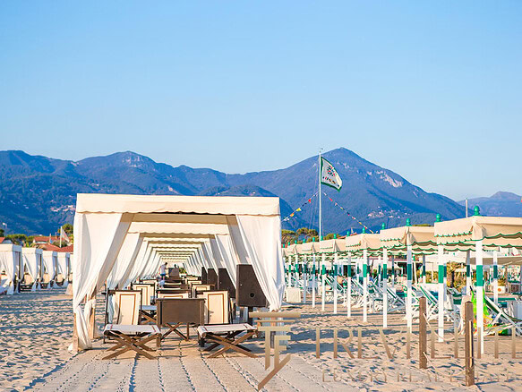 Вidовая сцена на пляже с белыми шатрами, шезлонгами и горами на фоне, идеальное место для отдыха у моря.