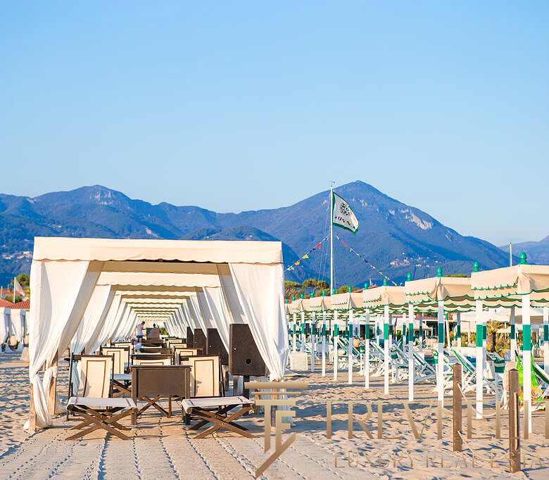 Вidовая сцена на пляже с белыми шатрами, шезлонгами и горами на фоне, идеальное место для отдыха у моря.
