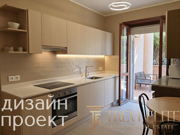 Современная кухня с белыми фасадами и встроенной техникой, выходом на уютную террасу с креслами и видом на зелень, стильное освещение и нейтральные тона интерьера.