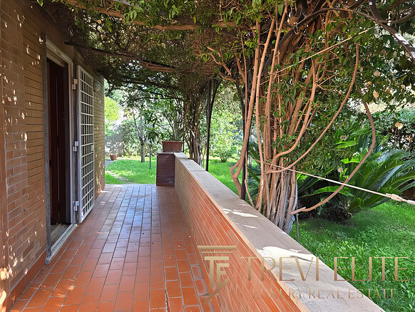 Уютная терраса возле дома с видом на зеленый сад и цветущие деревья, идеально подходит для отдыха и наслаждения природой в районе престижной недвижимости.