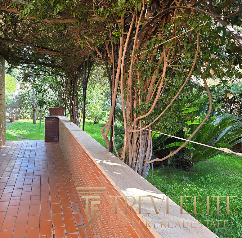 Уютная терраса возле дома с видом на зеленый сад и цветущие деревья, идеально подходит для отдыха и наслаждения природой в районе престижной недвижимости.