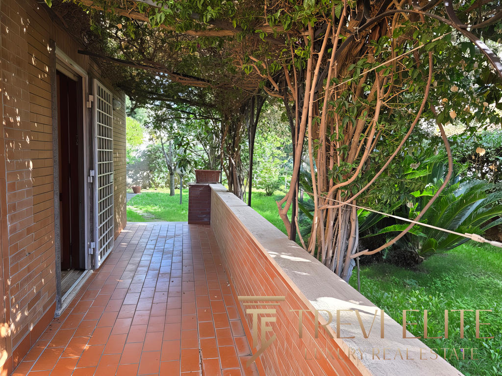 Уютная терраса возле дома с видом на зеленый сад и цветущие деревья, идеально подходит для отдыха и наслаждения природой в районе престижной недвижимости.