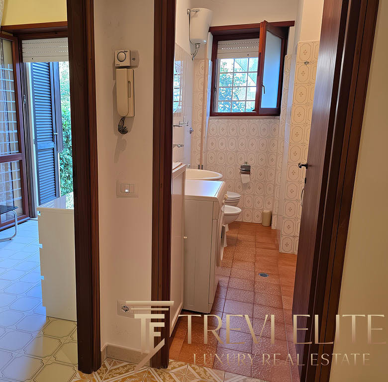 Вид из коридора в ванную комнату и балкон с видом на зеленый сад, оформленный в классическом стиле, с деревянными окнами и кафелем на полу, идеально подходит для комфортного проживания.