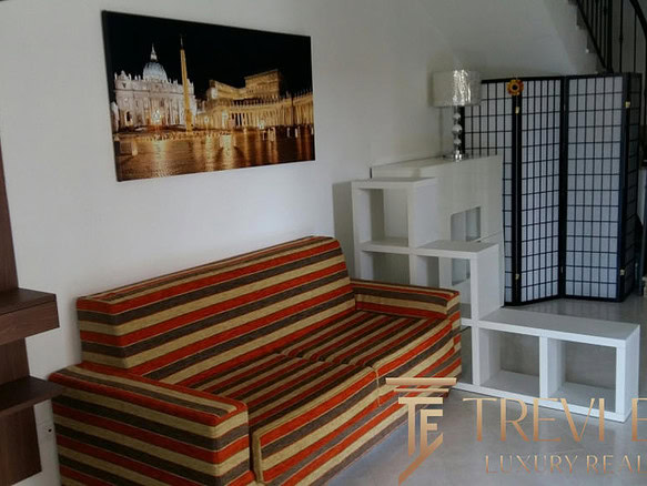 Высококачественное изображение уютного интерьера современного жилого пространства с комфортабельным диваном, декорированным панно, светильником и современной мебелью, которое демонстрирует профессиональные услуги агентства недвижимости Треви Элит.