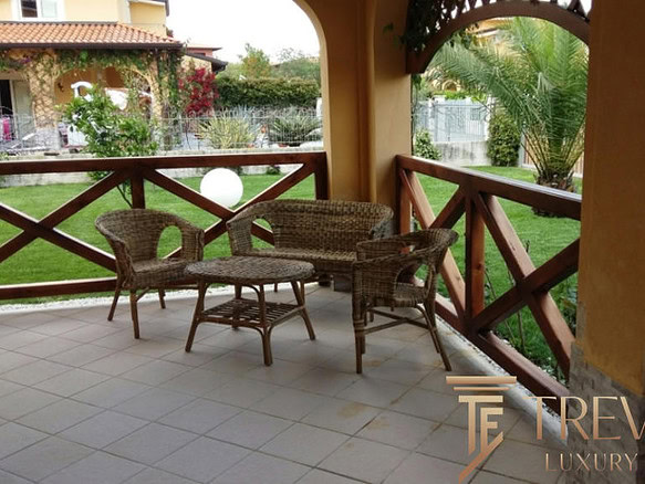 Уютное деревянное кресло и стол на террасе с видом на зеленый сад и соседние коттеджи. Идеальное место для отдыха и наслаждения природой. Надежное ограждение из дерева защищает пространство.