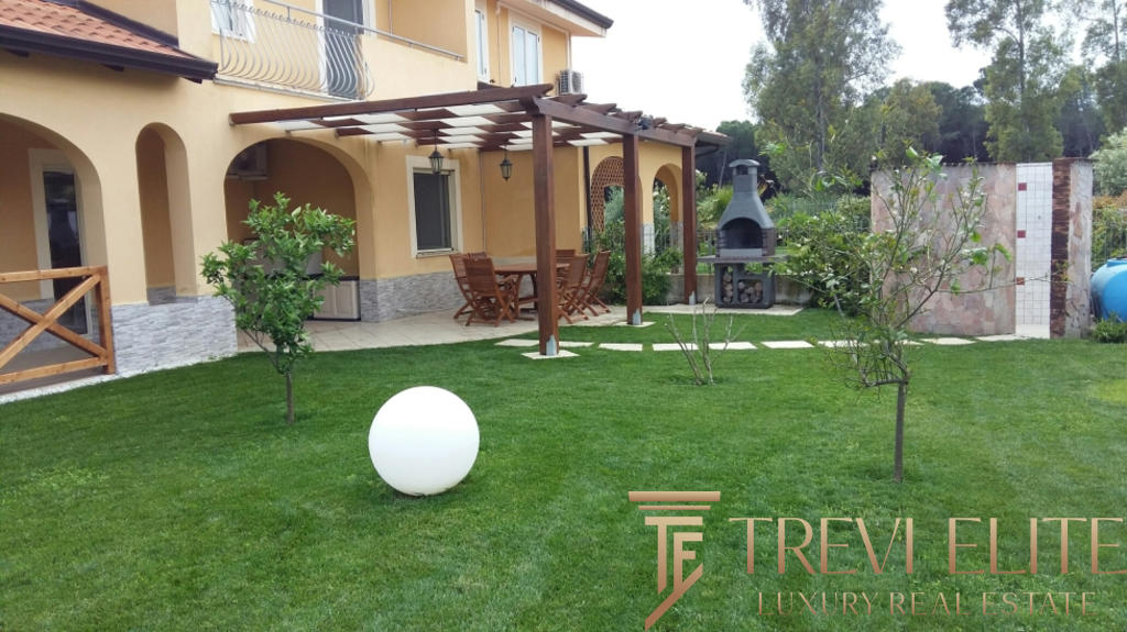 Красивый ухоженный двор с зоной барбекю и зеленой травой, окруженный деревьями и уютной террасой, идеально подходит для отдыха и проведения мероприятий.