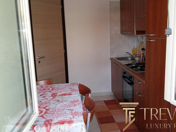 Миниатюрная кухня с деревянными шкафами и обеденным столом в светлой квартире на фоне окна.