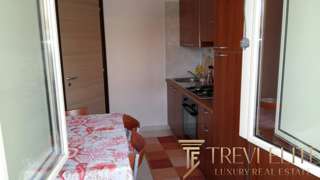 Миниатюрная кухня с деревянными шкафами и обеденным столом в светлой квартире на фоне окна.