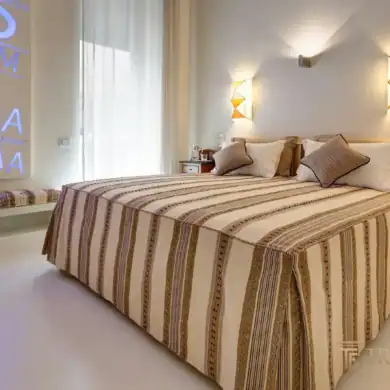 Master bedroom with striped bedcover, wall sconces, and modern art installation