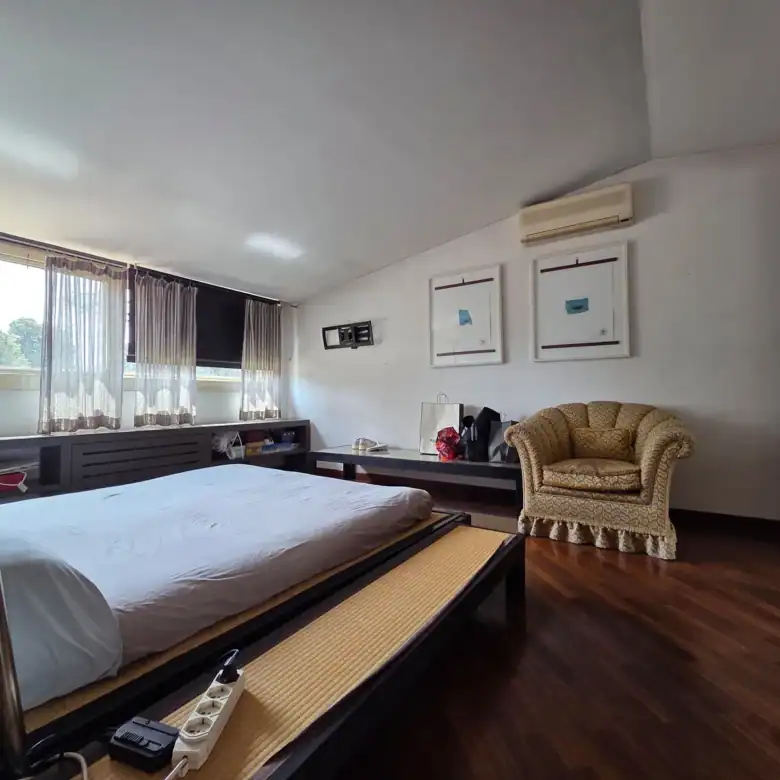 Spacious master bedroom with wood flooring, upholstered armchair, and garden views